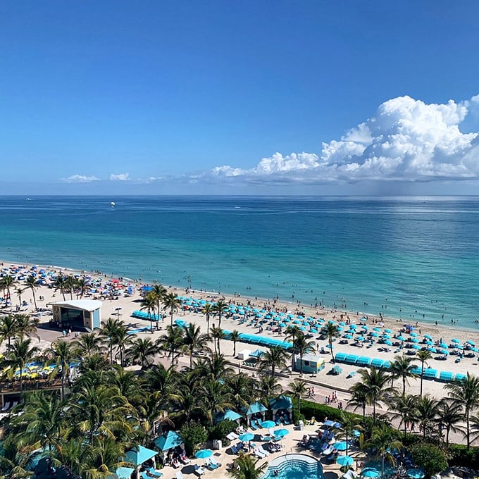 A bird's eye view of paradise: Turquoise waters meet golden sands, dotted with colorful umbrellas like a beachside Impressionist painting come to life.