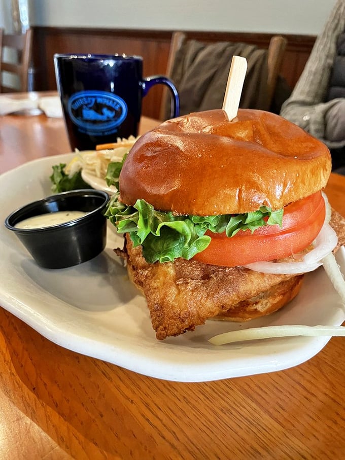 A perfectly crispy haddock sandwich towers proudly on its throne, accompanied by golden fries and house-made sauce.