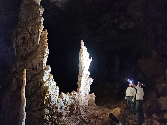 Nature's underground art gallery awaits! Two park rangers admire towering formations, their flashlights revealing millennia of geological masterpieces.