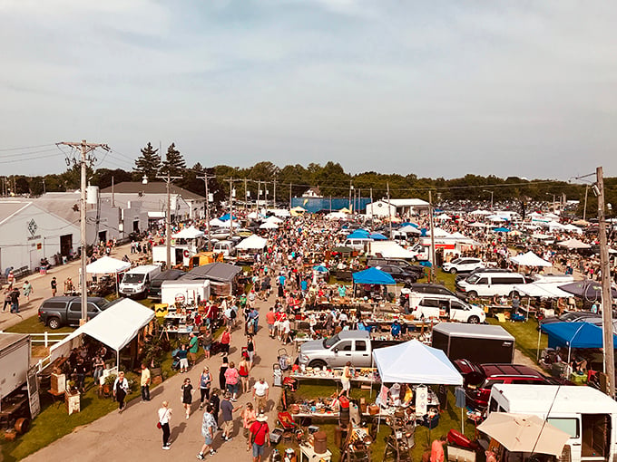 A bustling sea of tents, vehicles, and bargain hunters floods the grounds at the Elkhorn Antique Flea Market, where treasure seekers navigate a maze of vendors under a vast Midwestern sky.